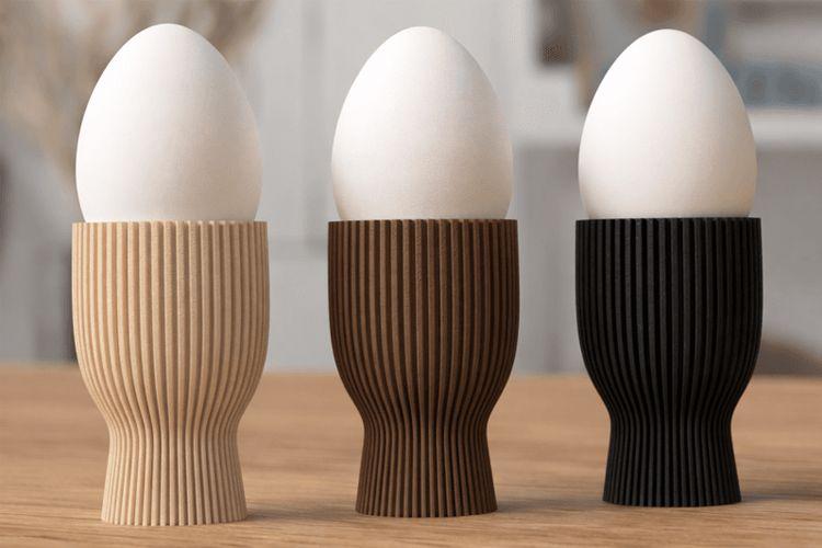 Tre egg i forskjellige eggkopper i lys, mørk og svart farge på et bord.
