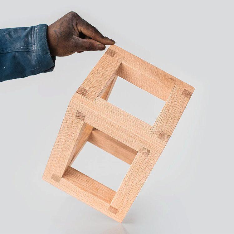 Hånd som holder en trestruktur i form av en 3D-kube med synlige skjøter og en lys bakgrunn.
