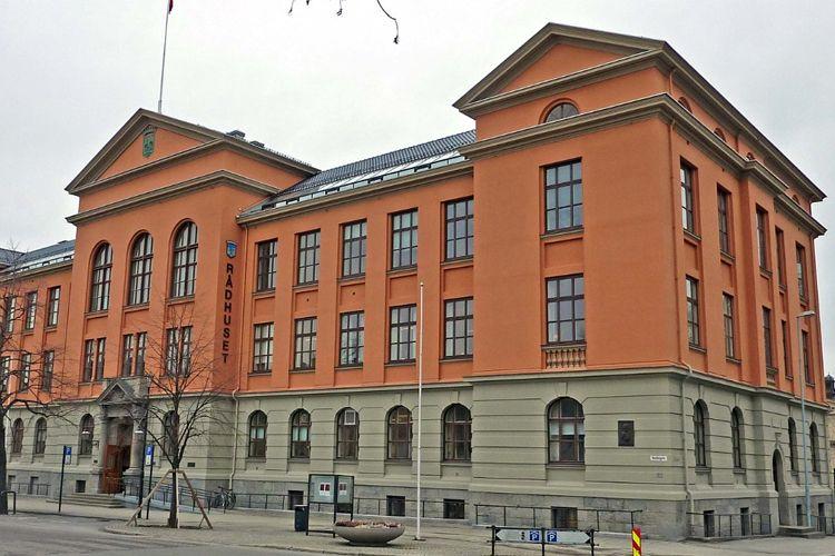 Rødt murbygg med store vinduer og flagg på taket, beliggende i en bygate.