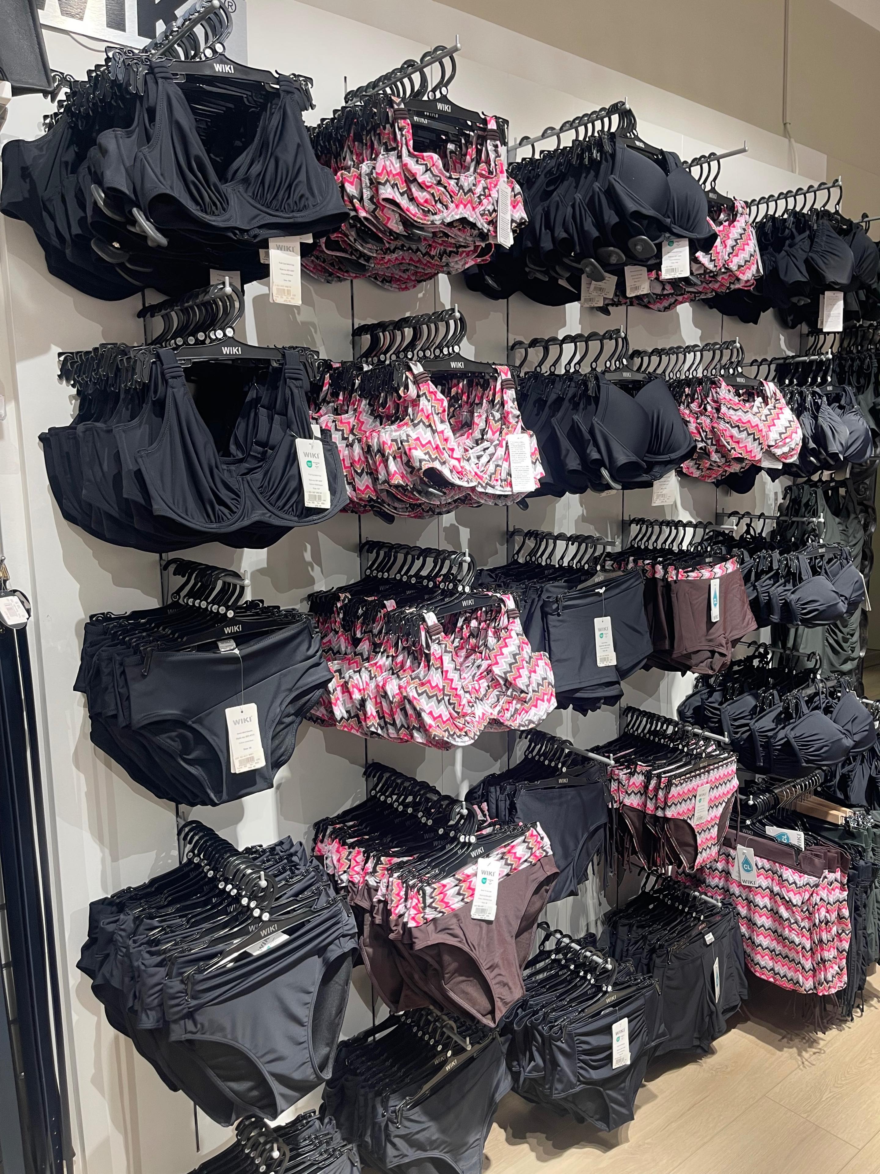 Bilde av en butikkvegg med forskjellige badetøy, inkludert svarte og rosa bikinier og truser.