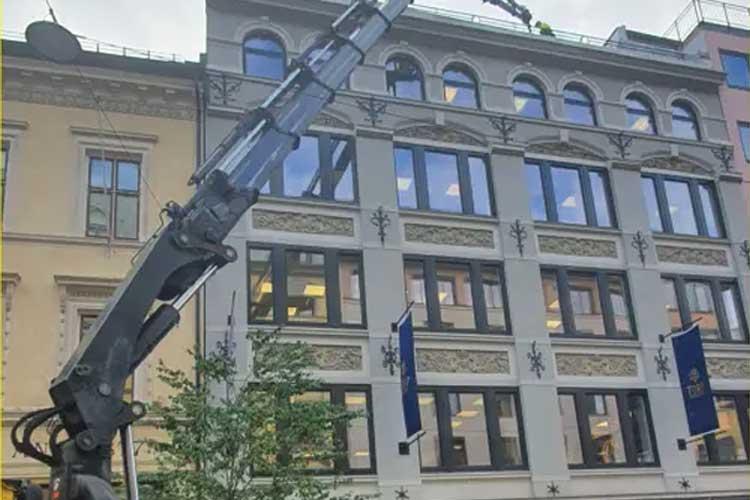 En kranarm strekker seg opp mot en bygning med store vinduer og dekorative detaljer.