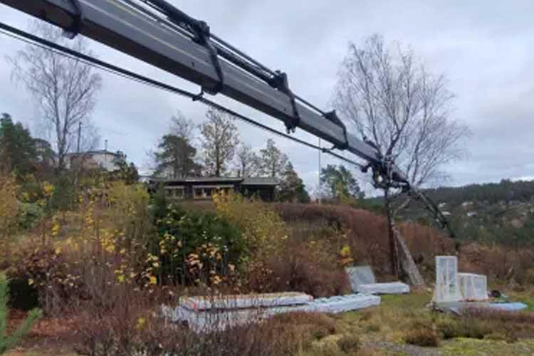 Kranarm som strekker seg over en hage med flere madrasser og trær i bakgrunnen.