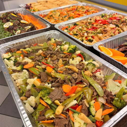 Fargerik buffet med grønnsaker, kjøtt og nudler i aluminiumsformer, perfekt for fest eller sammenkomst.