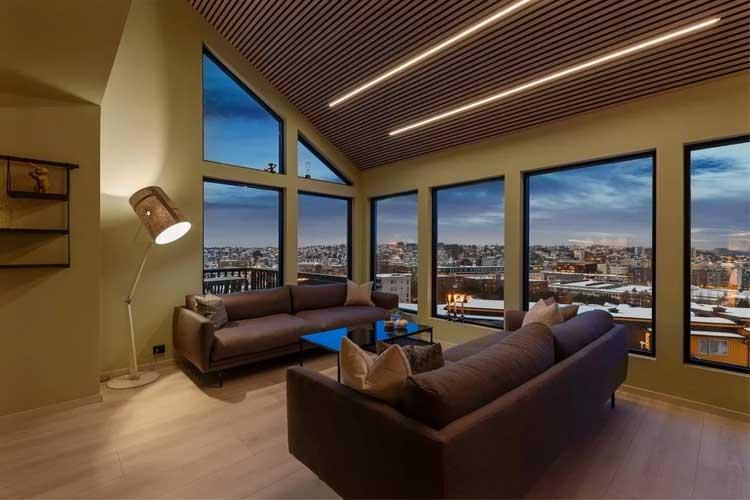 Moderne stue med store vinduer som gir utsikt over byen, to sofaer og et blått bord.