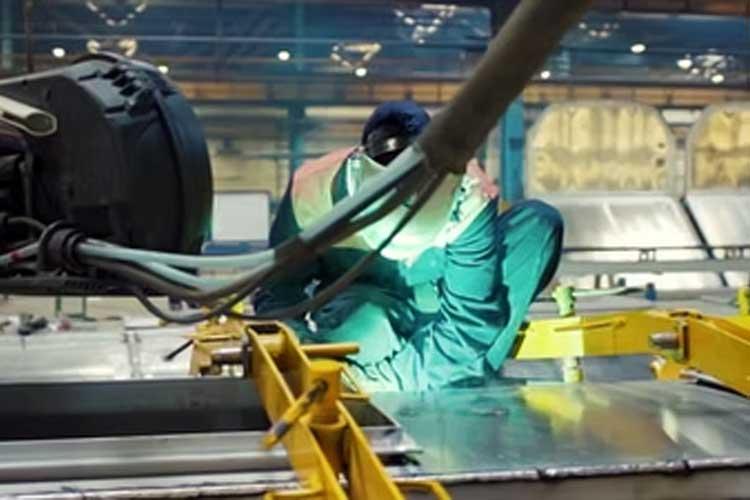 En sveiser i arbeid i en fabrikk, iført verneutstyr og fokusert på sveiseprosessen.