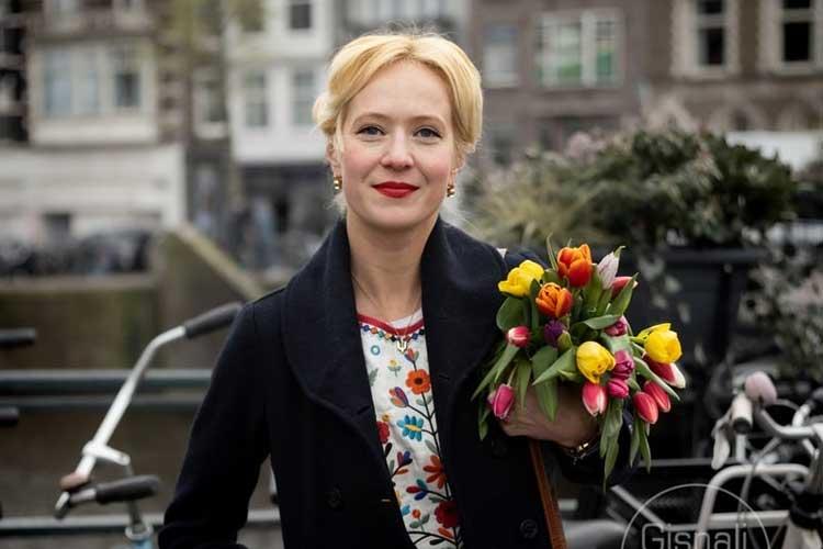 Kvinne med kort blond hår holder en bukett med fargerike tulipaner i en bygate.