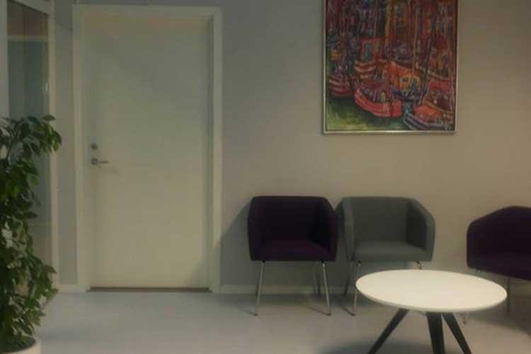 Moderne venterom med en hvit dør, to stoler i lilla og grå, samt et rundt bord i midten.
