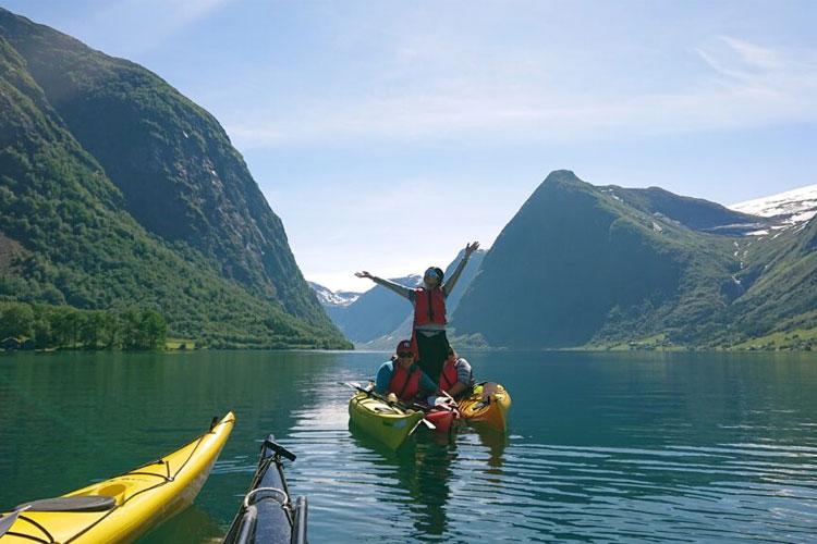 En gruppe mennesker padler i kajakk på en rolig innsjø omringet av fjell og grønn natur.