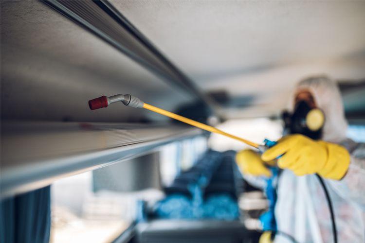 En person i beskyttelsesdrakt sprayer desinfeksjonsmiddel inne i en buss.