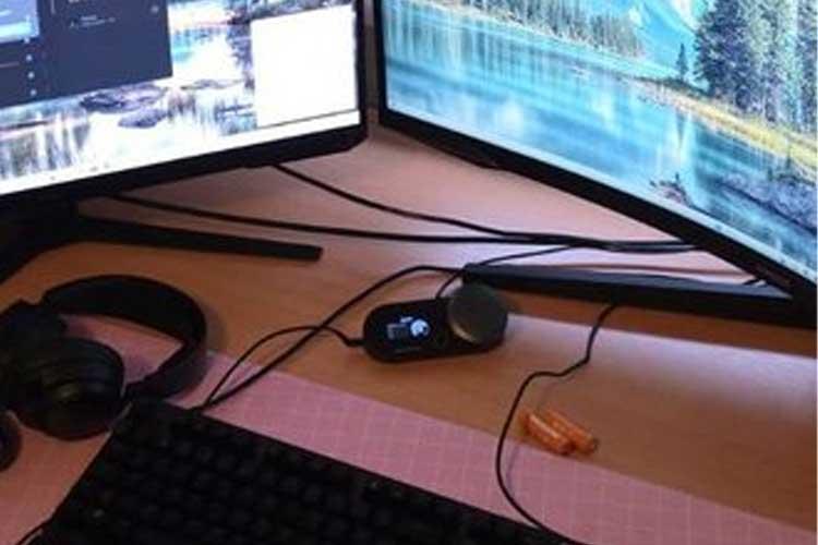 Et skrivebord med to dataskjermer, et tastatur, hodetelefoner og en liten høyttaler.