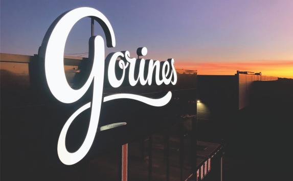 Lysende skilt med teksten "Gorines" mot en fargerik solnedgang.
