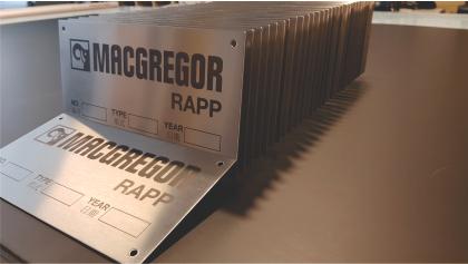 Flere metallplater med teksten "MACGREGOR RAPP" og plass for navn og år. Plater stablet på et bord.