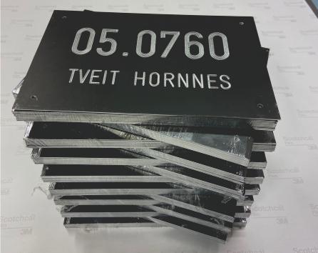 En stabel med svarte skilt med hvite bokstaver som viser "05.0760 Tveit Hornnes".