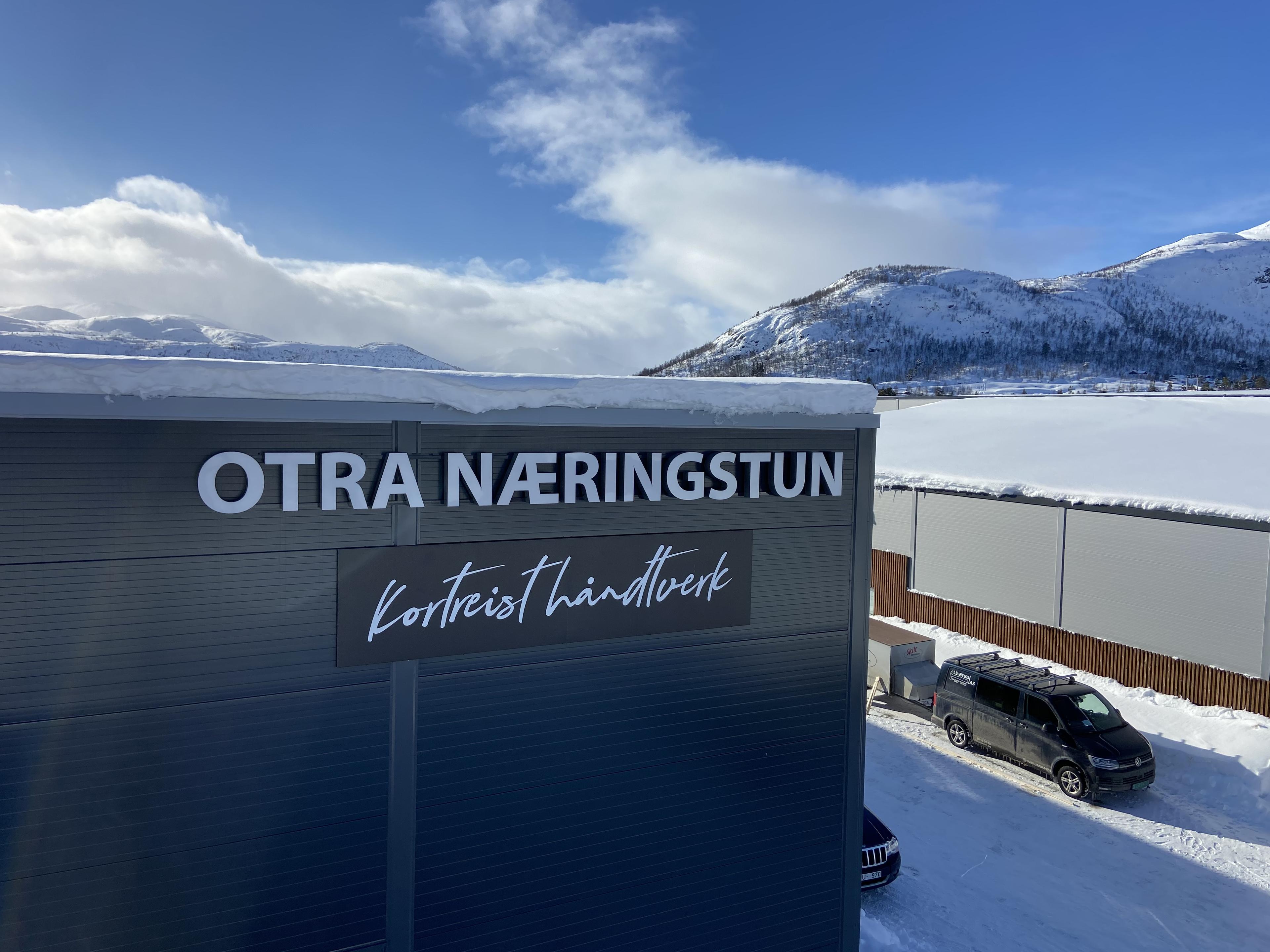 Bygning med teksten "OTRA NÆRINGSTUN" og "Korteist Kinnhus" på en snødekt bakgrunn i fjellandskap.