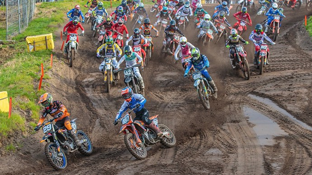 En gruppe motocrosskjørere konkurrerer i et støvete terreng, med mange sykler i aksjon.