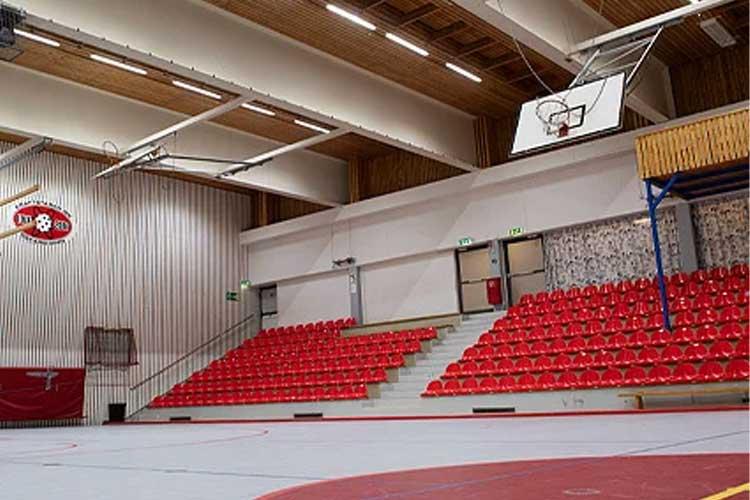 Innendørs basketballbane med røde tribuner og en basketballkurv hengende fra taket.