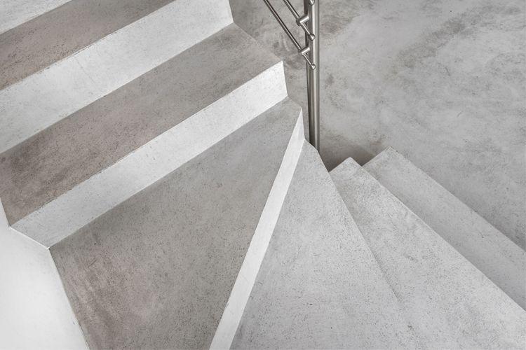 Trappen med betongtrinn og metallrekkverk som fører nedover i et moderne interiør.