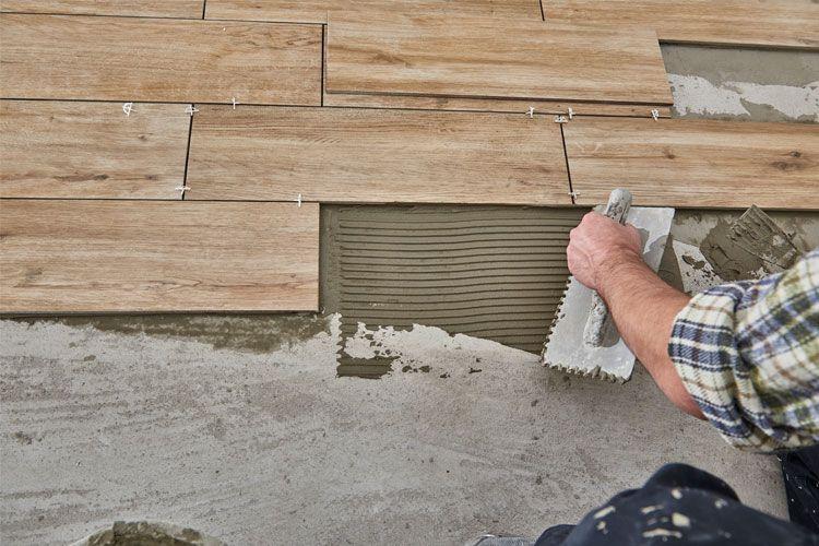 En hånd som legger fliser på gulvet med mønstret mørtel i en byggeprosess.