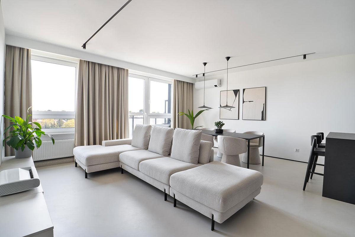 Moderne stue med lys sofa, spisebord, planter og store vinduer som slipper inn naturlig lys.
