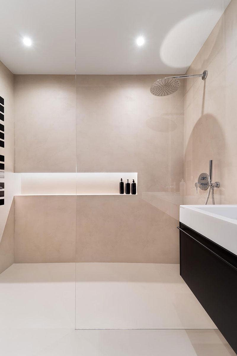 Moderne bad med dusj, badekar og stilige svarte flasker på en hylle. Lys beige fliser og minimalistisk design.