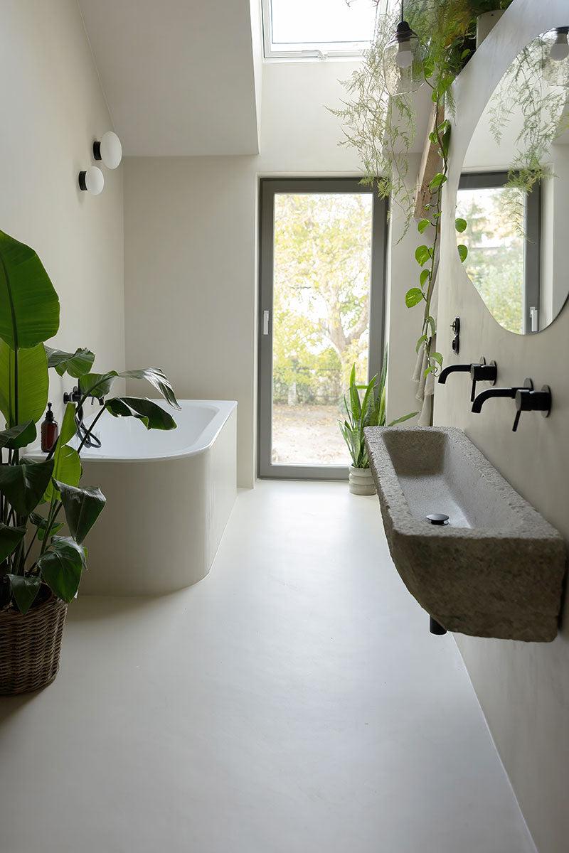 Moderne bad med badekar, steinvask, planter og store vinduer som slipper inn naturlig lys.