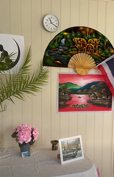 Innendørs interiør med en klokke, malerier, en vifte, en palme og blomster på et bord.