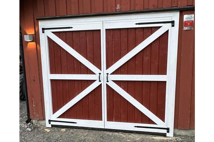 Rød låvedør med hvite detaljer og kryssmønster, plassert på en bygning med trepanel.