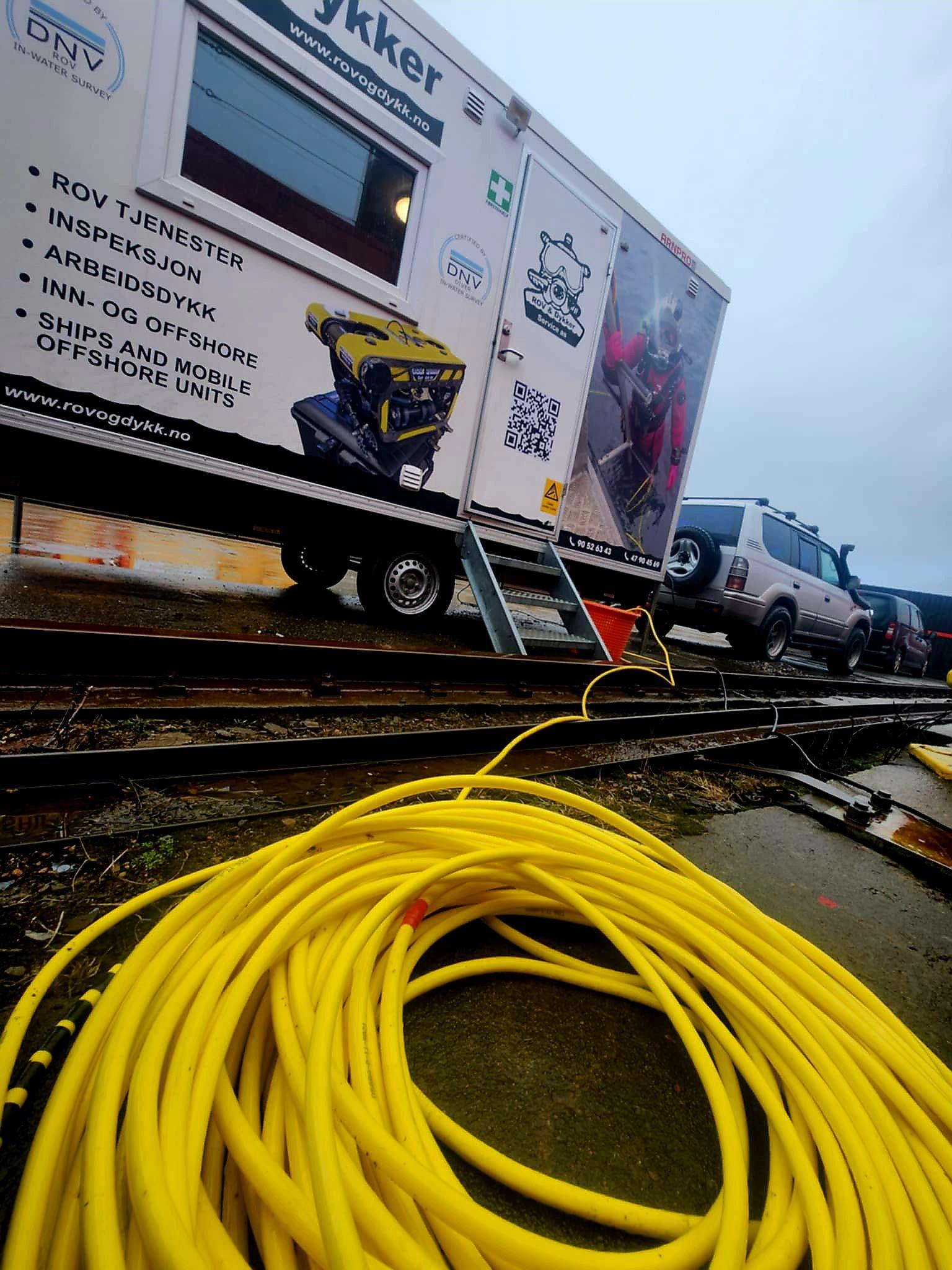 Gul slange ligger på bakken foran en trailer med verktøy og utstyr til redning og vedlikehold.
