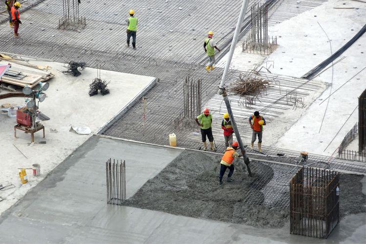 Arbeidere som heller betong på en byggeplass, med stålstenger og byggeutstyr i bakgrunnen.