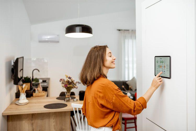 Kvinne som justerer en smart enhet på veggen i et moderne kjøkken med treinnredning.
