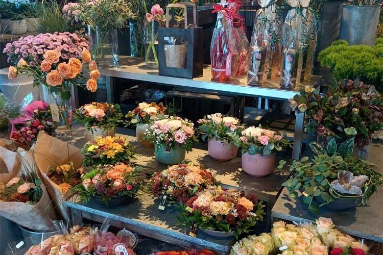 Blomsterbutikk med fargerike blomsteroppsatser, potteplanter og dekorative buketter på hyller og bord.