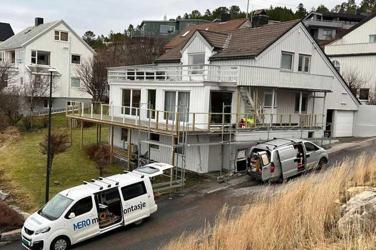 Hus under oppussing med stillas, en varebil parkert foran, og en annen bil med verktøy ved siden av.