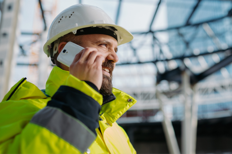 En byggarbeider i hjelm og refleksjakke snakker i telefonen på en byggeplass.
