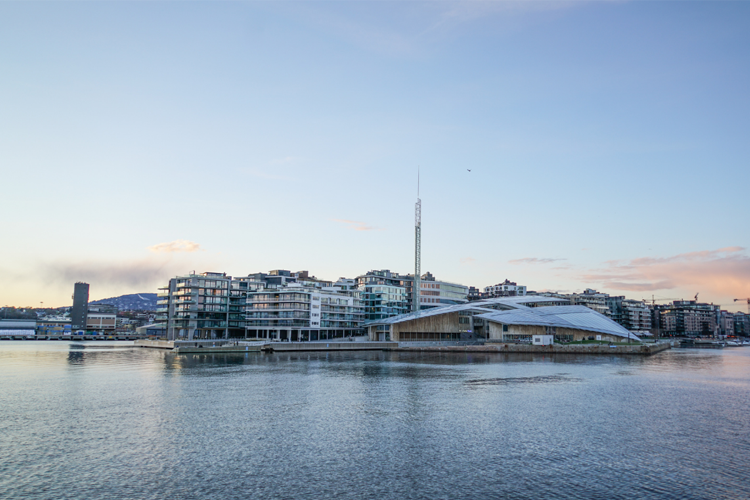 Moderne bygninger ved vannkanten i Oslo, med en karakteristisk spire og vakker himmel i bakgrunnen.