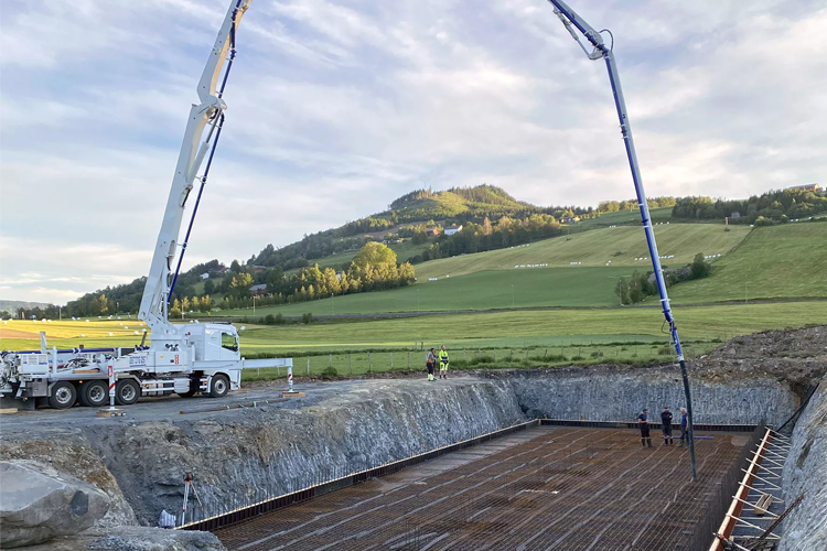 Betongpumping på byggeplass med gravd ut område og fjellbakgrunn i norsk landskap.