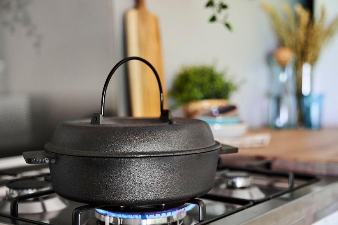 En svart støpejernsgryte på en gasskomfyr med flammer under, i et moderne kjøkkenmiljø.