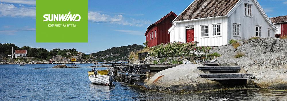 Bilde av en kystlinje med hvite og røde hus, båter ved bryggen og frodig natur i bakgrunnen.
