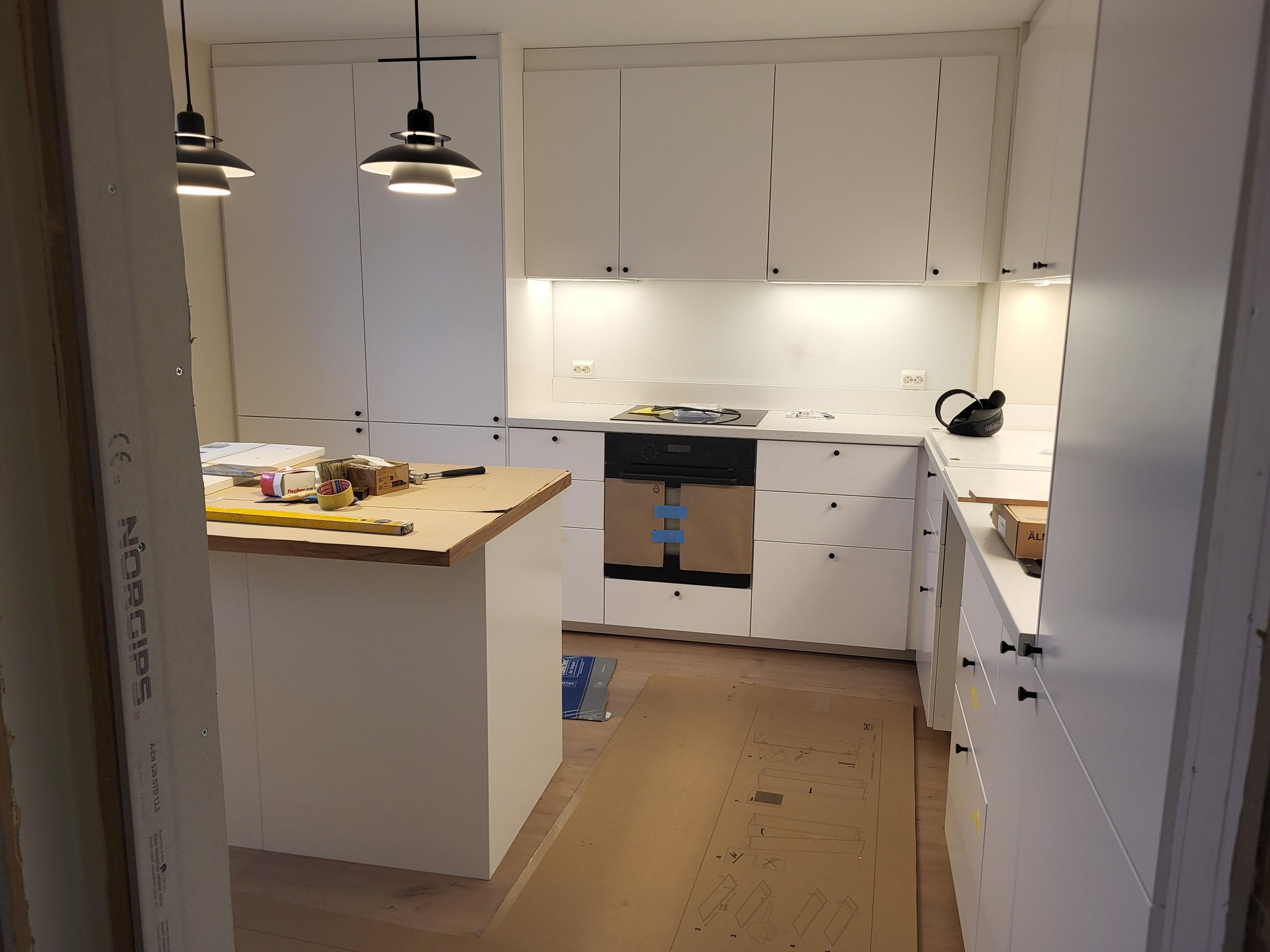 Moderne kjøkken med hvite skap, trebenkeplate og stilige taklamper.