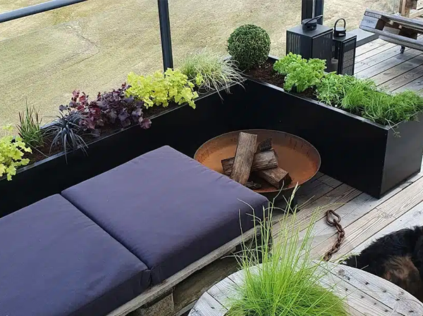En balkong med planter, en sitteplass med puter og en peis med ved.