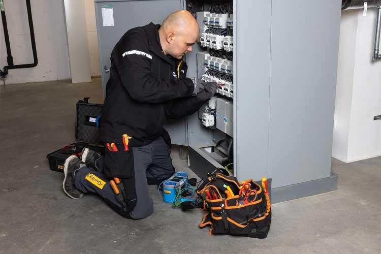 En elektriker som arbeider med sikringsskapet i en bygning, med verktøy og utstyr rundt seg.