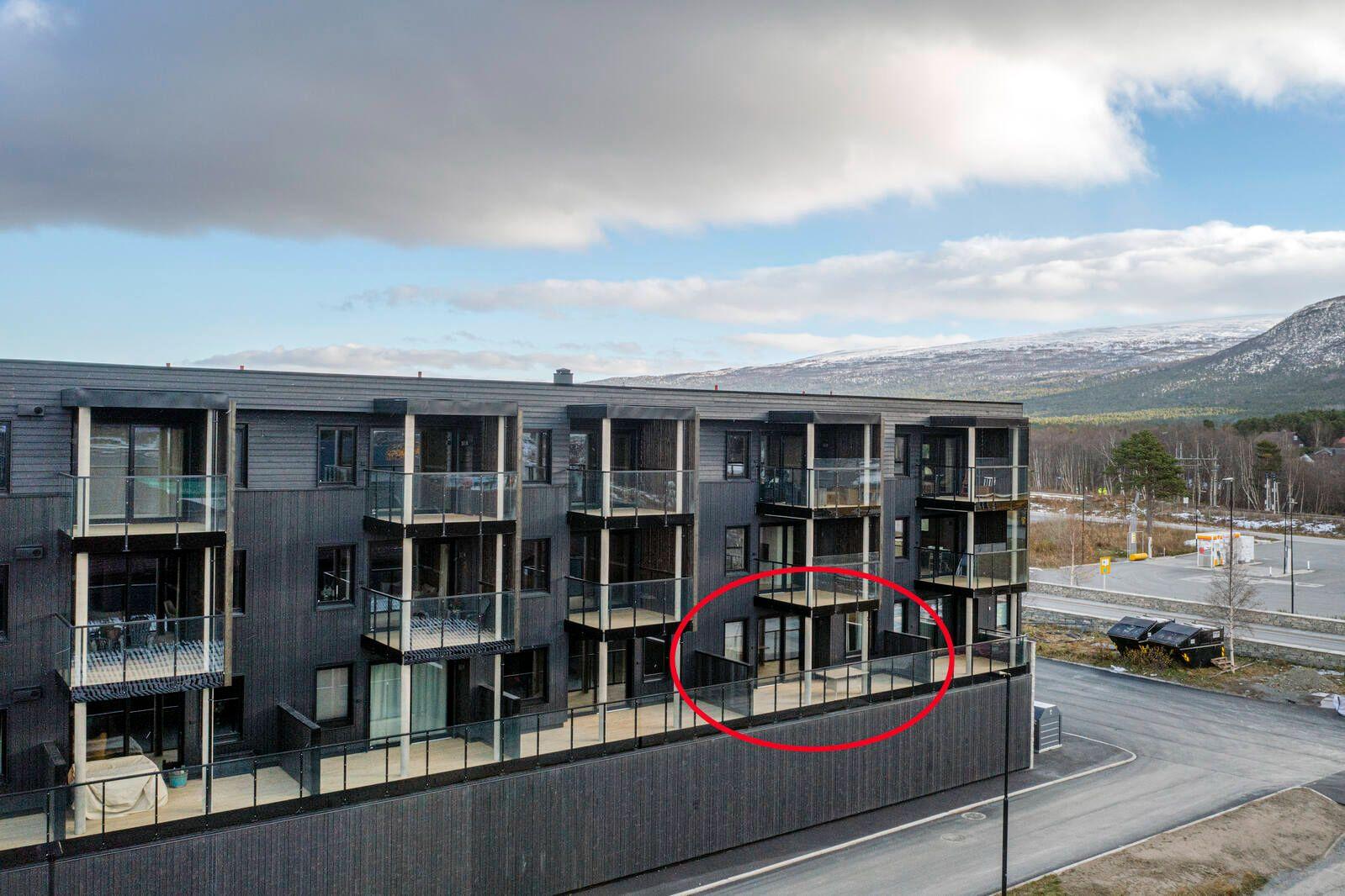 Moderne leilighetskompleks med balkonger, beliggende i naturskjønt område med fjell i bakgrunnen.