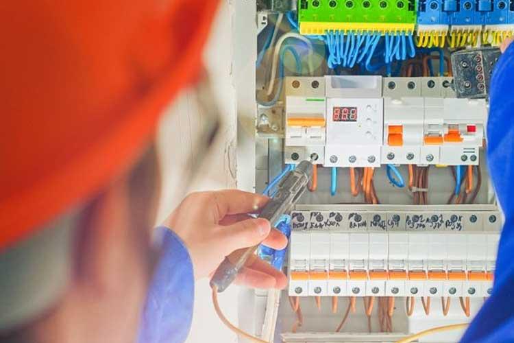 En elektriker jobber med elektriske ledninger i et sikringsskap, med verktøy i hånden.