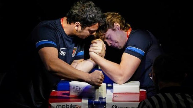 To menn som konkurrerer i armwrestling, med fokus på styrke og intensitet under kampen.