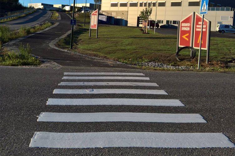 Fotografi av en fotgjengerovergang med hvite striper, nær en bygning og en vei som fører oppover.