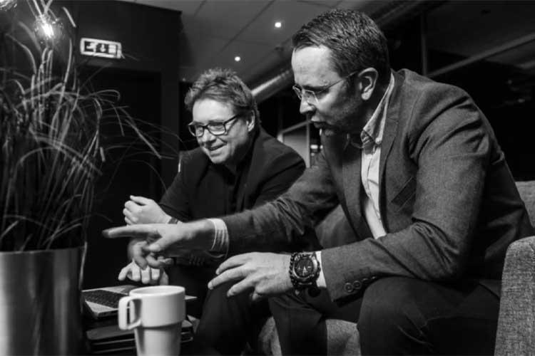 To personer sitter sammen i en moderne setting, diskuterer og peker på en skjerm, med en plante i bakgrunnen.