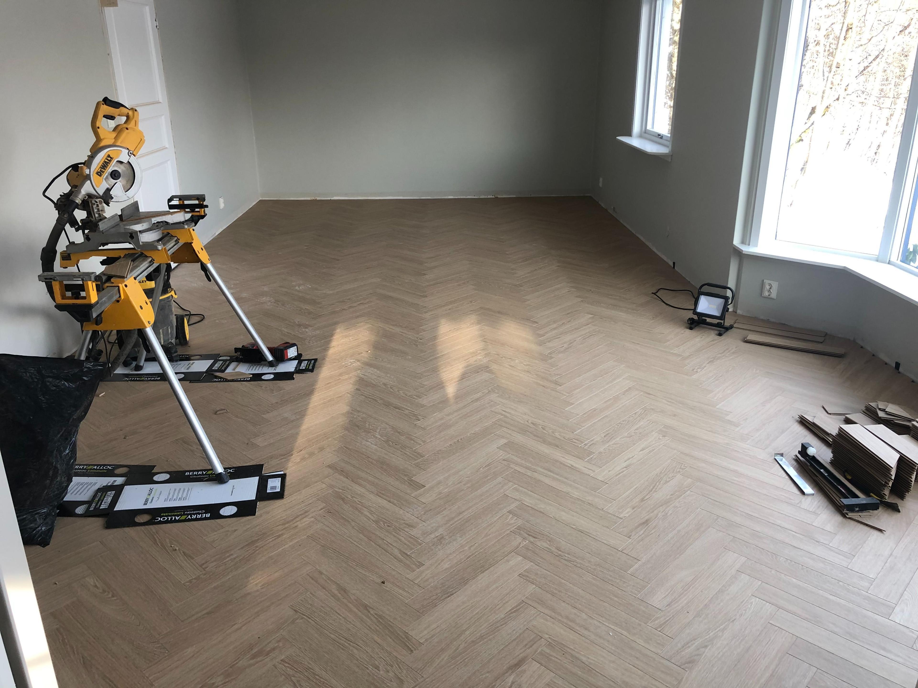 Rom med parkettgulv, verktøy som en gulvsliper og arbeidslamper, samt store vinduer som slipper inn naturlig lys.