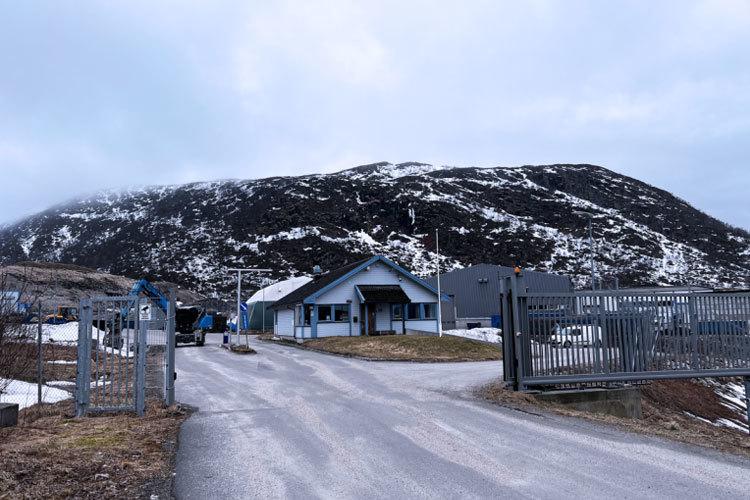 En vei som fører til en blå bygning med fjell i bakgrunnen, delvis dekket av snø.