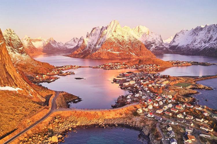 En vakker soloppgang over fjorder og fjell i Lofoten, med en liten landsby ved vannkanten.