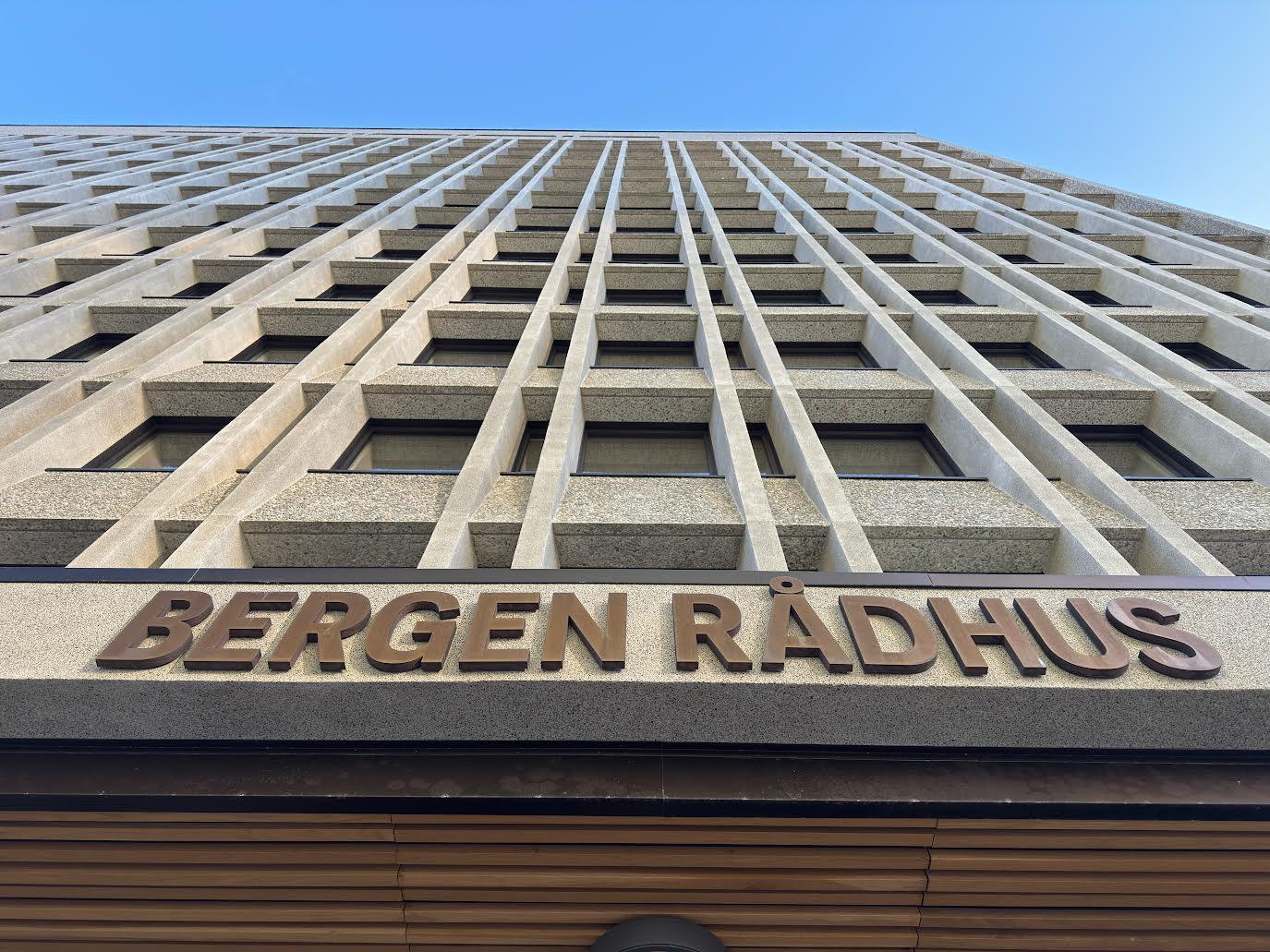 Bergen Rådhus med moderne arkitektur og tydelig skilt, fotografert fra bakken opp mot bygningens fasade.