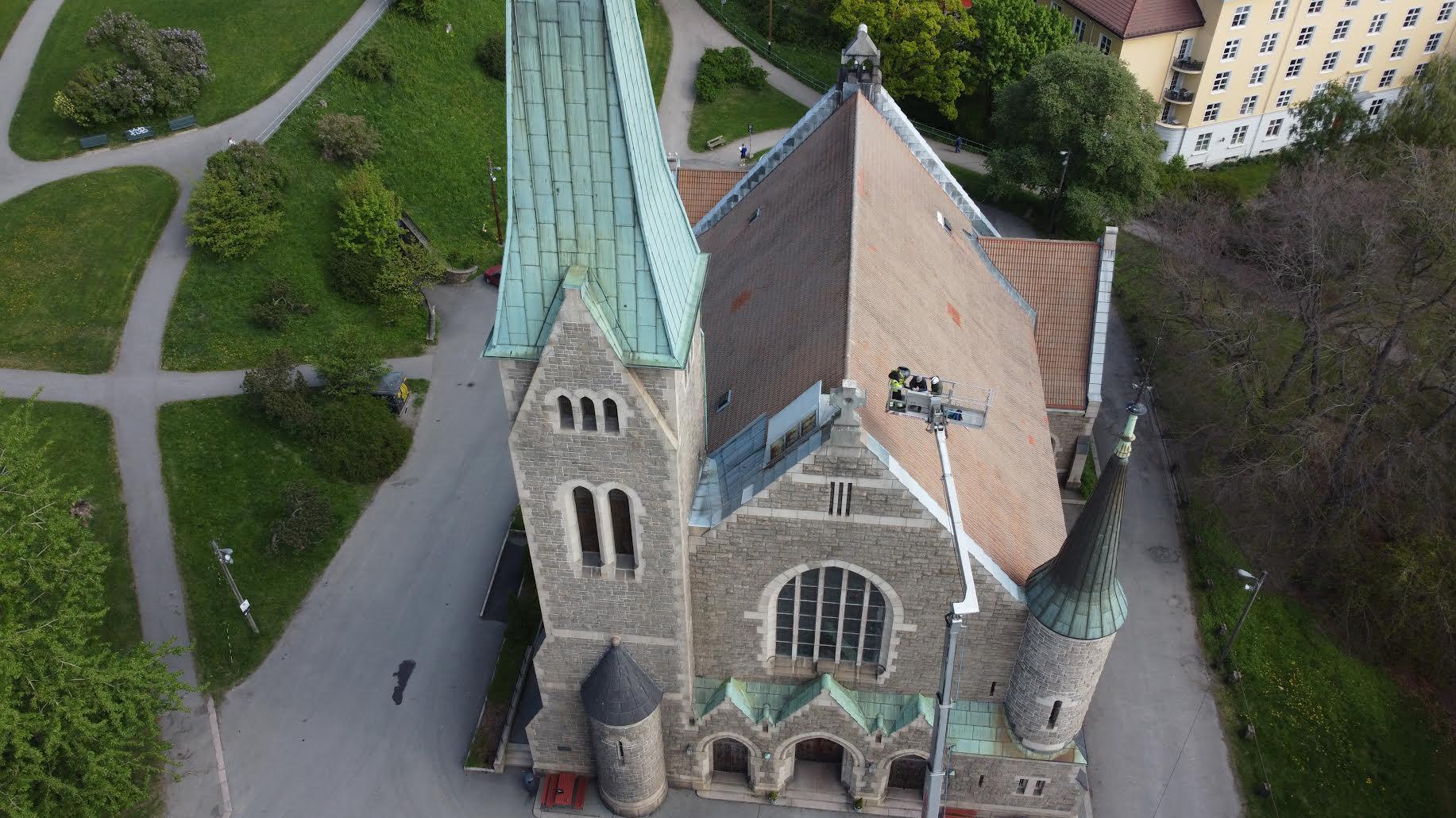 En oversiktsbilde av en steinkirke med grønt tak, omgitt av parker og bygninger.